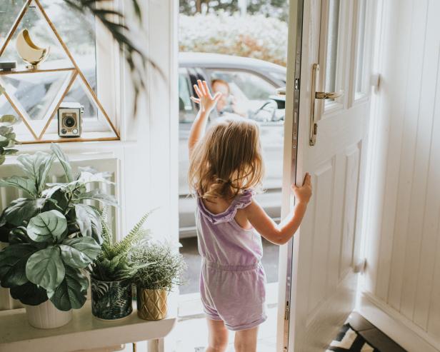 Cute little girl waving out the door in a sunny hallway.