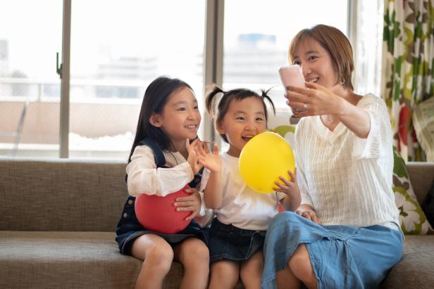 A candid photo of a Korean mother and her young daughters video calling with her smartphone.