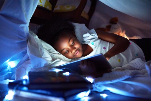 Cropped shot of an adorable little girl using a digital tablet while lying in bed
