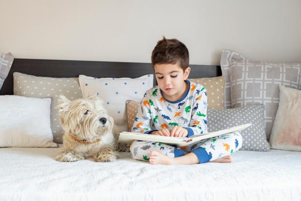 A little boy reading book to his westy dog puppy on the bed