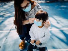 Young mother putting on surgical mask for little daughter in the playground to prevent the spread of cold and flu and viruses