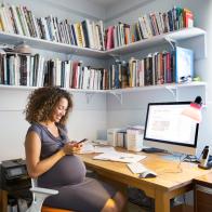 A mixed race pregnant woman works from home sitting at her desk using computer.