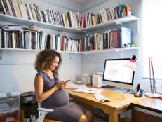 A mixed race pregnant woman works from home sitting at her desk using computer.