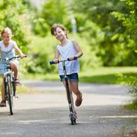 Girls drive scooter and ride bike in the park during summer vacation