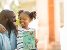 Happy Father's Day.  Little girl gives homemade card to her dad in front yard of family home.  African descent family.