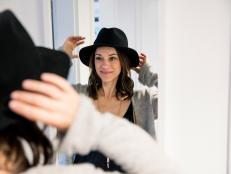 Mature woman standing in front of mirror , putting on a hat