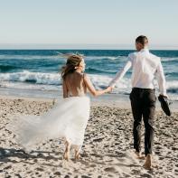 Rear view of bride and groom running on the beach