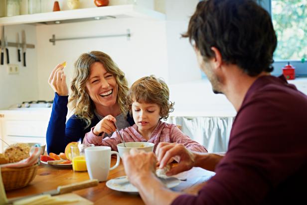 Happy family of three enjoying breakfast at table in domestic kitchen