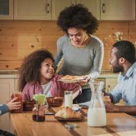 Happy African American woman serving breakfast to her family in dining room. Focus is on mother and daughter.