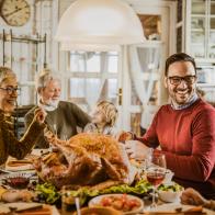 Happy multi-generation family communicating while having Thanksgiving lunch in dining room. Focus is on man and senior woman.