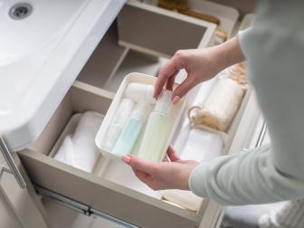 Top view female housewife organizing bathroom amenities and toiletries in open drawer under sink. Woman enjoying housework bath storage use Marie Kondo's method. Modern keeping space organize interior
