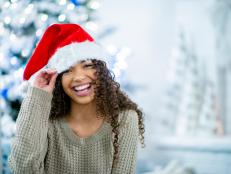 A teenage girl of African descent is in her home at Christmas time. She is laughing while wearing a santa hat.