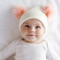 Cute adorable baby child with warm white and pink hat with cute bobbles. Happy baby girl on white background and looking at the camera. Close-up for xmas holiday and family concept.