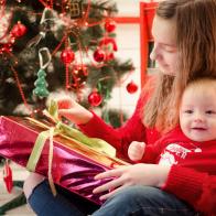 Teen sister with her baby brother in red clothes in Christmas time open gifts and presents near the Christmas tree in red tones interior. Great difference in age between siblings.