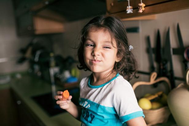 Pretty 4 years girl eating carrot in kitchen, sitting on her kitchen counter