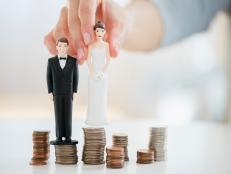 Mixed race woman balancing bride and groom statues on coin stacks