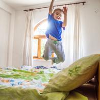 Little boy is jumping on the bed. He is flying!