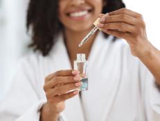 Beauty And Skincare. Smiling Black Woman Holding And Opening Bottle With Moisturizing Face Serum, Making Skin Treatment At Home, Closeup