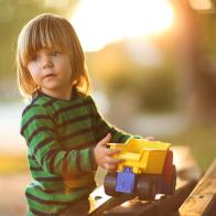 Cute blonde boy playing with his truck in the park on the bench,sunlight