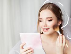 Bride Face Make up Finish. Bridal Wedding Makeup Close up. Skin Foundation Application. Happy Beauty Model holding Blush Brush looking at Mirror putting Makeup. Perfect Smooth Skin Color Texture. White Background