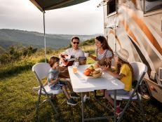 Happy family having fun while singing at picnic table by the camper trailer in nature. Man is playing a guitar.