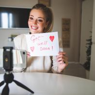 Woman in video call with a friend holding a message to get well soon