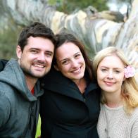 Three siblings, two sisters and a brother hug and smile together in the country