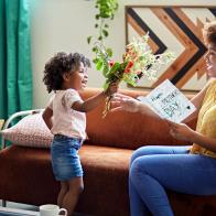 Side view of 3 year old Afro-Caribbean girl giving mother in mid 20s bouquet of flowers and homemade card.