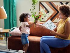 Side view of 3 year old Afro-Caribbean girl giving mother in mid 20s bouquet of flowers and homemade card.