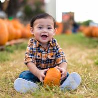 9 month old baby sits at a pumpkin patch at she start of October.
