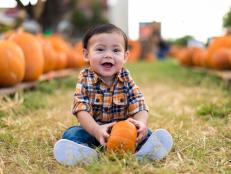 9 month old baby sits at a pumpkin patch at she start of October.