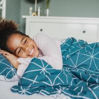 a little African American carefree girl is laying in bed