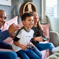 Candid portrait of mature man sitting on sofa with boy and girl, having fun, winning, competition