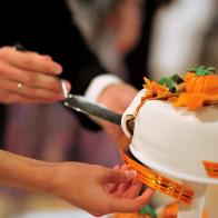 The bride and groom cut a beautiful wedding white cake decorated with orange pumpkins. Halloween autumn wedding concept