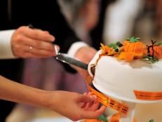 The bride and groom cut a beautiful wedding white cake decorated with orange pumpkins. Halloween autumn wedding concept