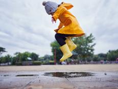 Cute and playful female child jumping in a puddle of water on the street wearing yellow rubber boots and a raincoat.