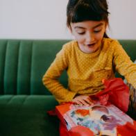 Happy little Eurasian girl unwrapping birthday present at home