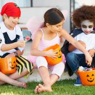 Children dressed in Halloween costumes holding candy buckets while sitting down