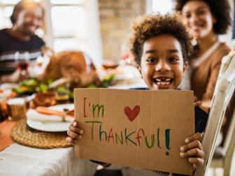 Happy African American girl holding 'I'm thankful' sign and looking at camera during Thanksgiving meal with her parents.