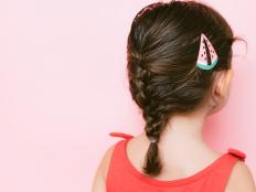 Back view of little girl with braid and hair clip against pink background