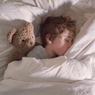 A boy sleeping alone in his parent's bed with his teddy bear.