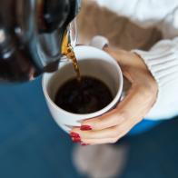 Close-up of a woman pouring herself hot filter coffee to a mug while staying at home.