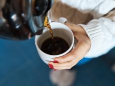 Close-up of a woman pouring herself hot filter coffee to a mug while staying at home.
