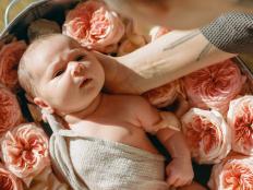 Small cute neborn beautiful baby bathes in warm water with pink flowers and petals in the hands of a caring mother. The concept of baby care and aromatherapy.