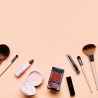 Top view of set for makeup application on peach background. Soft brushes, lipsticks, face powder, blushes and nail polish. Flat lay style. Cosmetic banner with copy space. Using decorative cosmetics is a trendy way to brighten up the days after coronavirus pandemic of the year 2020