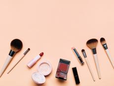 Top view of set for makeup application on peach background. Soft brushes, lipsticks, face powder, blushes and nail polish. Flat lay style. Cosmetic banner with copy space. Using decorative cosmetics is a trendy way to brighten up the days after coronavirus pandemic of the year 2020