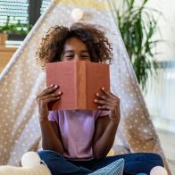 Portrait of young African American girl playing on the floor and holding a book