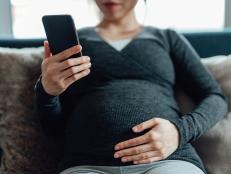 Cropped shot of pregnant woman having a video call on smartphone while touching her belly, sitting on sofa at home. Using telemedicine app on smartphone to monitor her health.