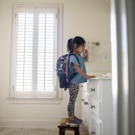 Young girl with backpack brushing her teeth in bathroom