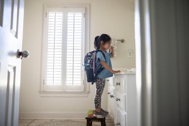 Young girl with backpack brushing her teeth in bathroom